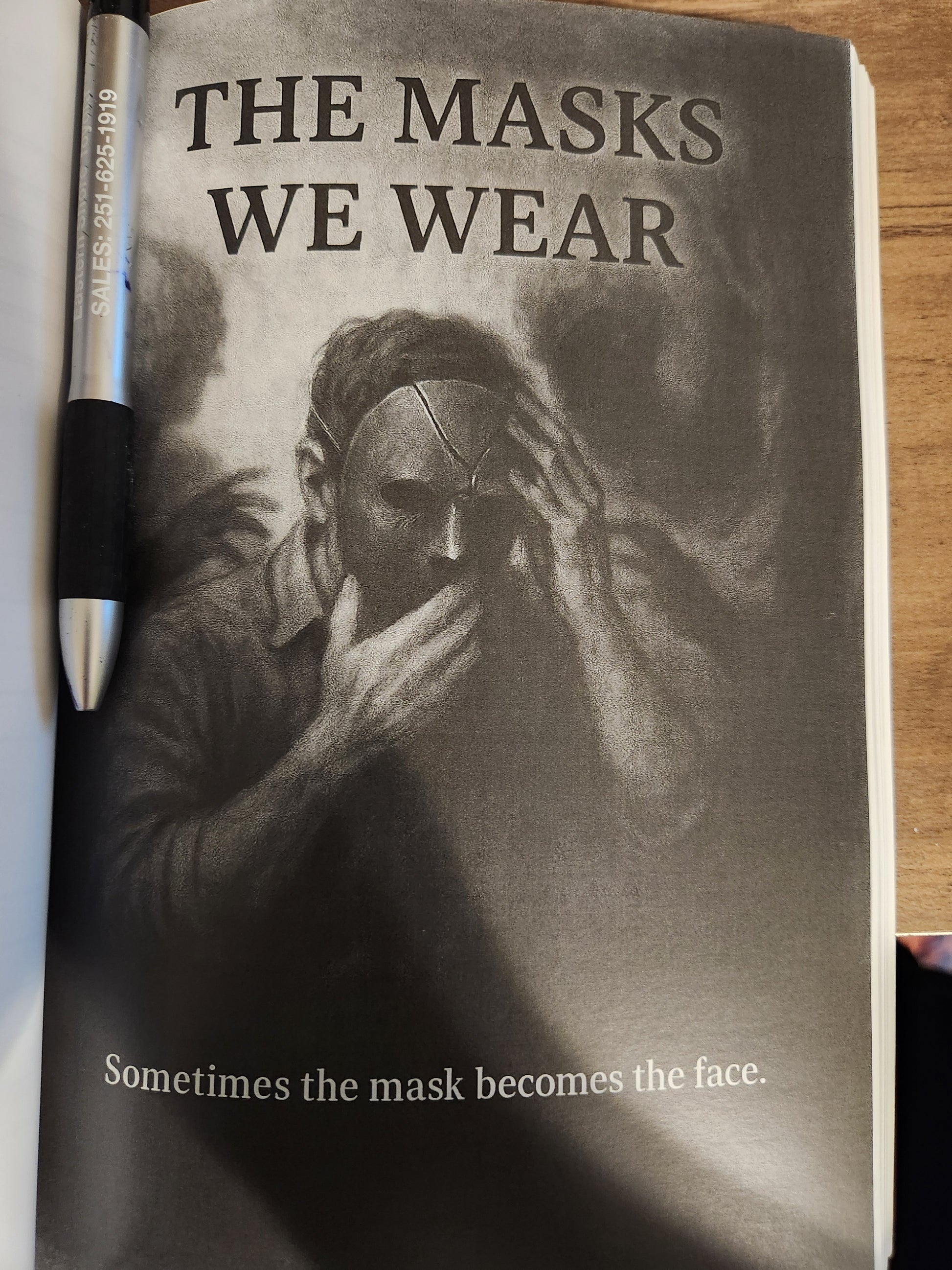 'The Masks We Wear' with a pen on a wooden surface